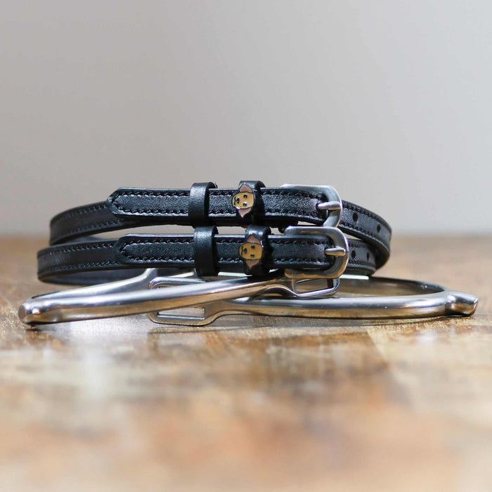 Coiled black leather Labrador spur straps resting on a silver spur, golden dog face charms