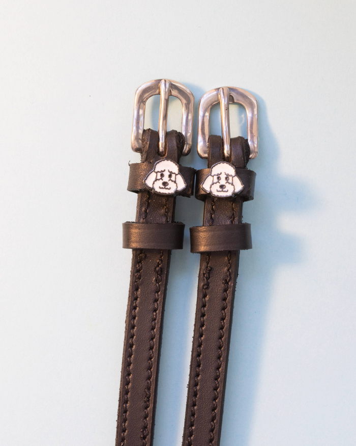 Dark brown ManeJane spur straps with white poodle face charms on off-white