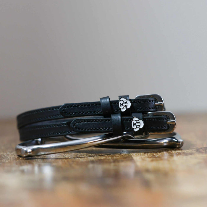 Black leather poodle spur straps stacked on a silver spur on wood, close-up