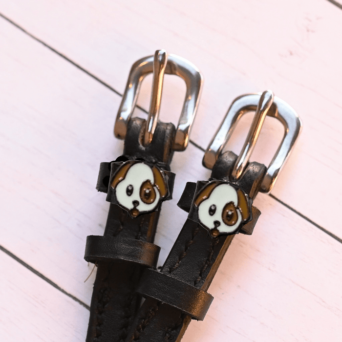Two puppy face charms on dark brown leather spur straps over pink planks