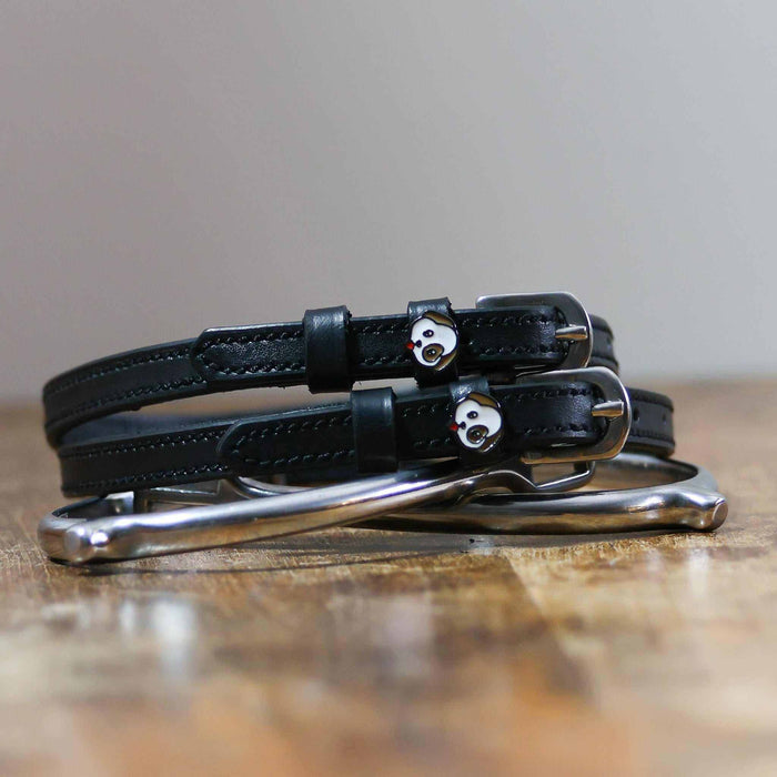 Black leather puppy face spur straps coiled beside a spur on wood