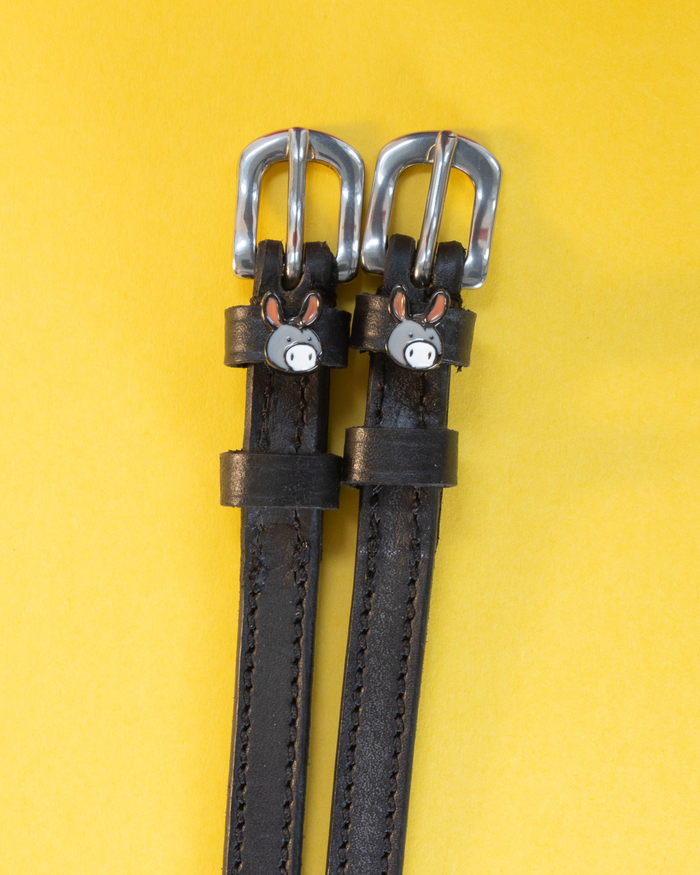 Black leather ManeJane spur straps with silver buckles and grey donkey face charms on yellow