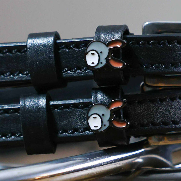 Close-up of grey donkey face charms on black leather ManeJane spur strap keepers