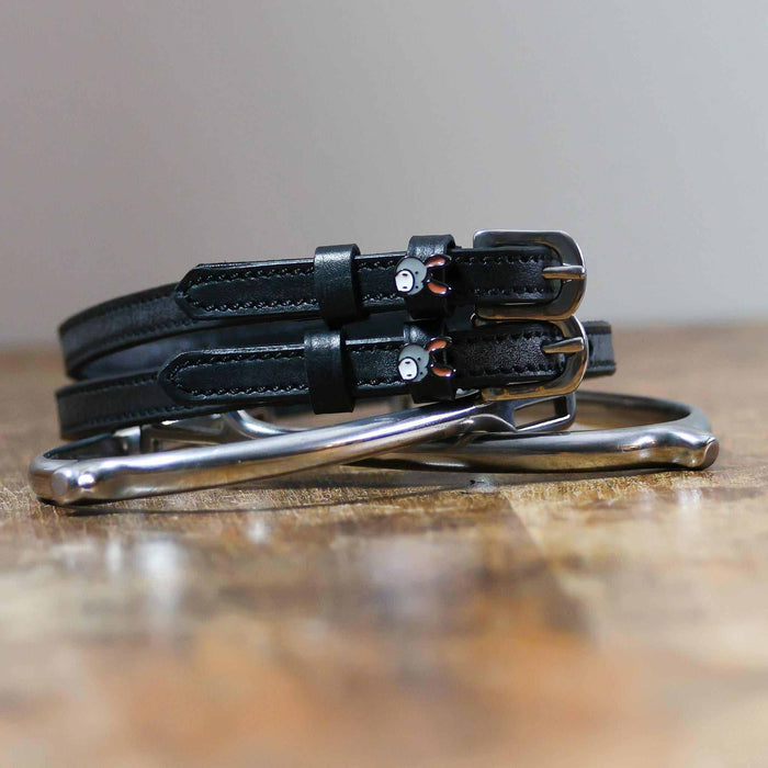 Black leather donkey spur straps coiled beside a silver stirrup on a wooden surface