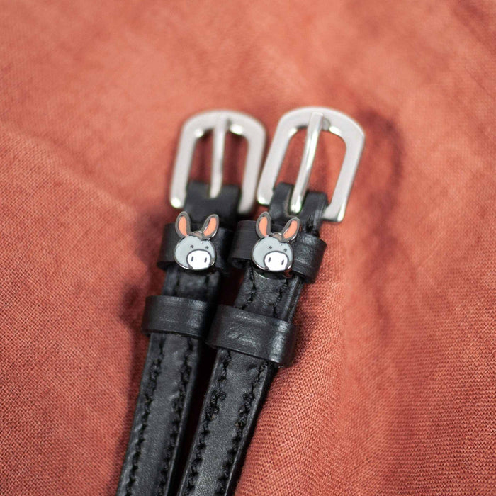 Black leather donkey spur straps with silver buckles angled on a rust linen background