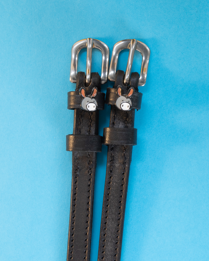 Black leather donkey spur straps with silver buckles on a light blue background