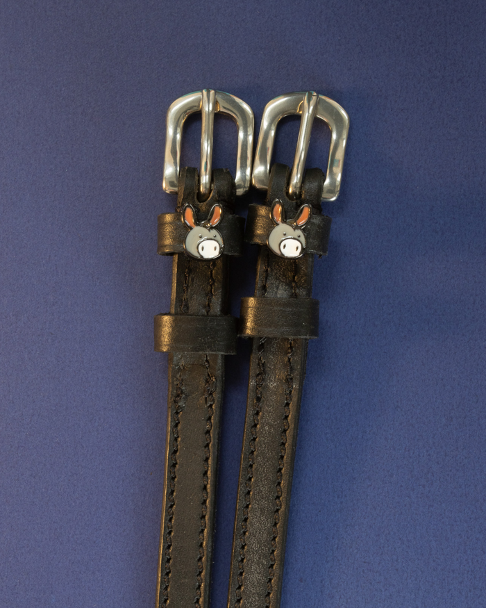 Black leather donkey spur straps with silver buckles on a navy blue background