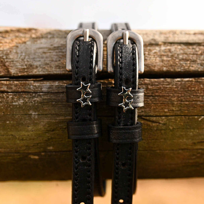 ManeJane double star spur straps hanging over a weathered wooden fence rail