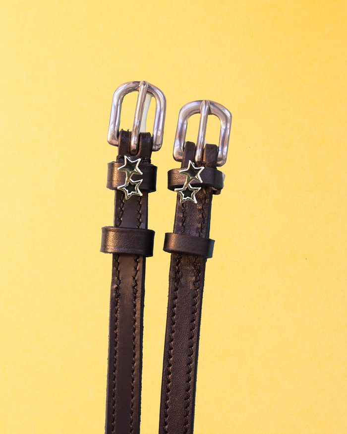Pair of dark brown double star spur straps flat-laid on a yellow background