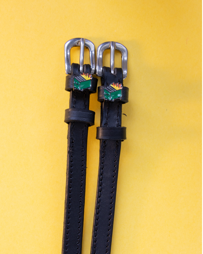 Pair of black leather dumpster fire spur straps with silver buckles on yellow