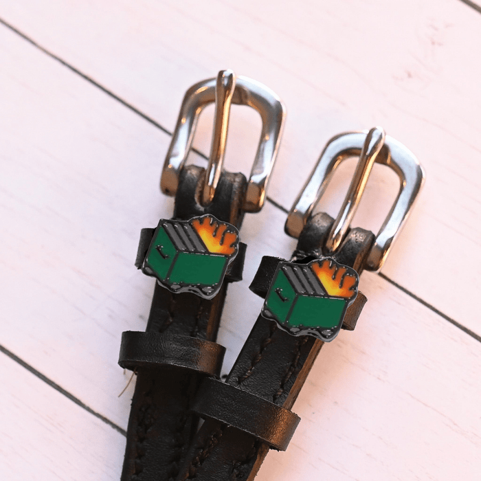 Close-up of dumpster fire charms on black leather spur straps on pink wood planks
