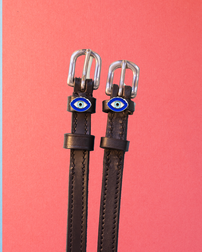 ManeJane evil eye spur straps with blue charms flat on a coral pink background