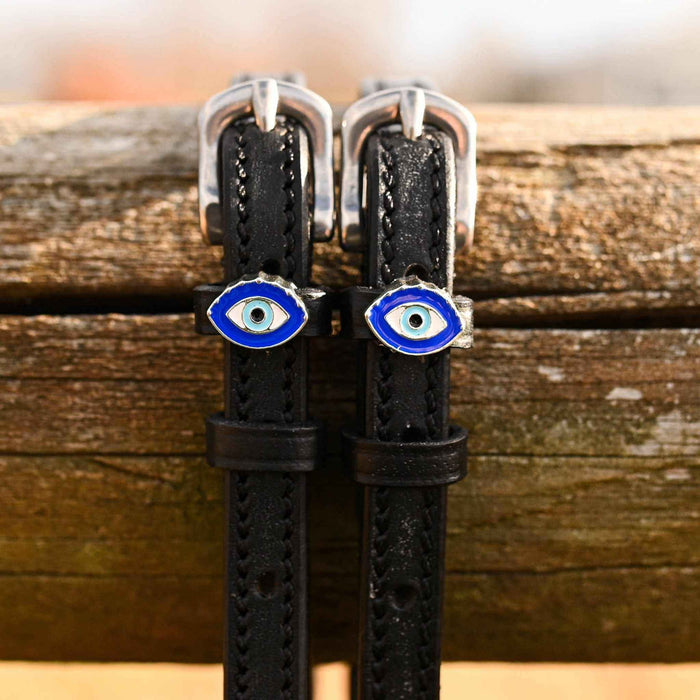 Close-up of blue evil eye charms on black leather spur straps over a wooden rail