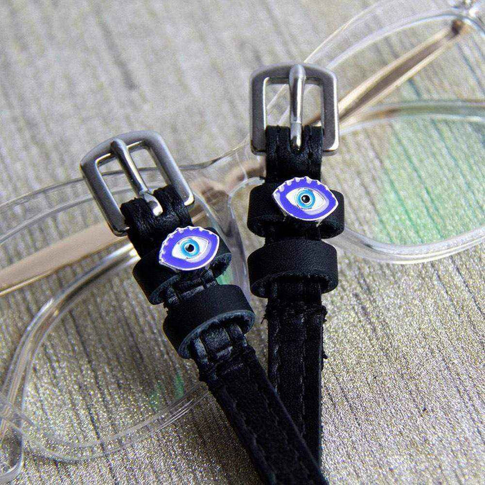 Blue evil eye spur straps resting on clear eyeglasses, ManeJane leather spur straps