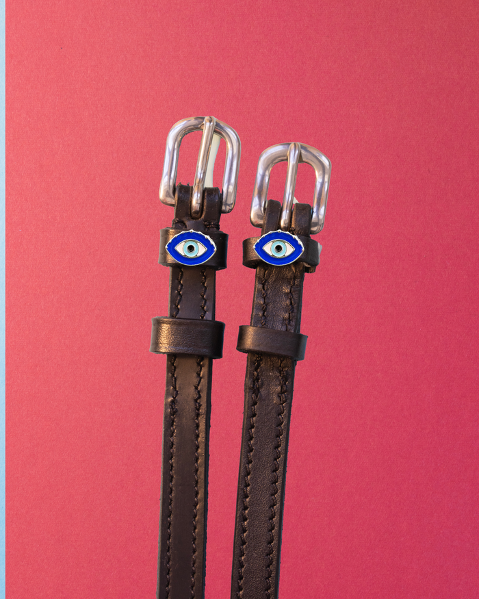 Dark leather evil eye spur straps with silver buckles on a red background