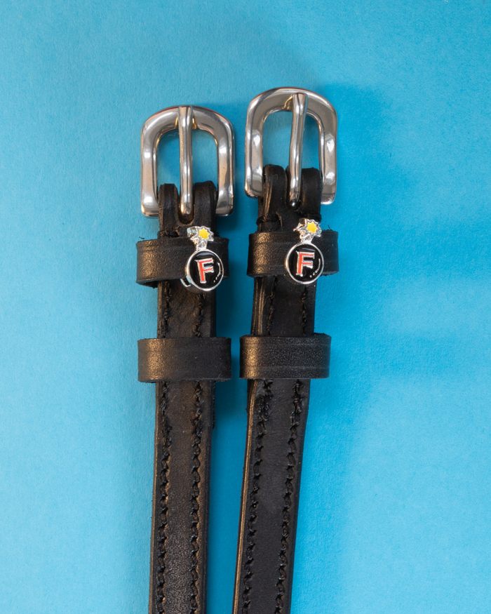 Black leather ManeJane F Bomb spur straps with silver buckles and red F-bomb charms on blue