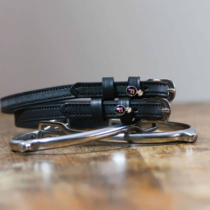 F Bomb spur straps coiled beside silver spurs on a wooden table with red bomb charms