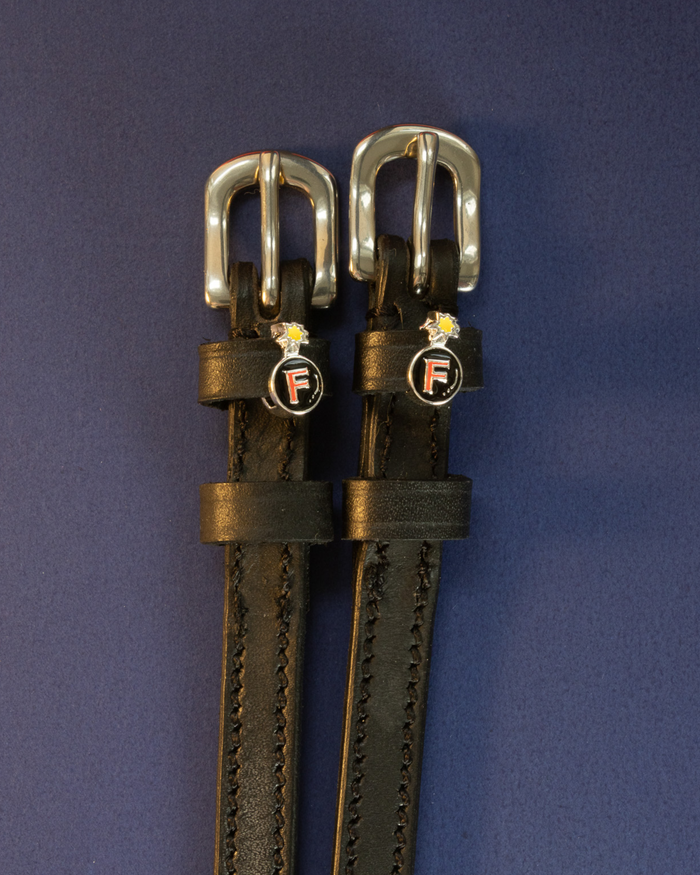 Black leather F Bomb ManeJane spur straps with silver buckles on a navy background