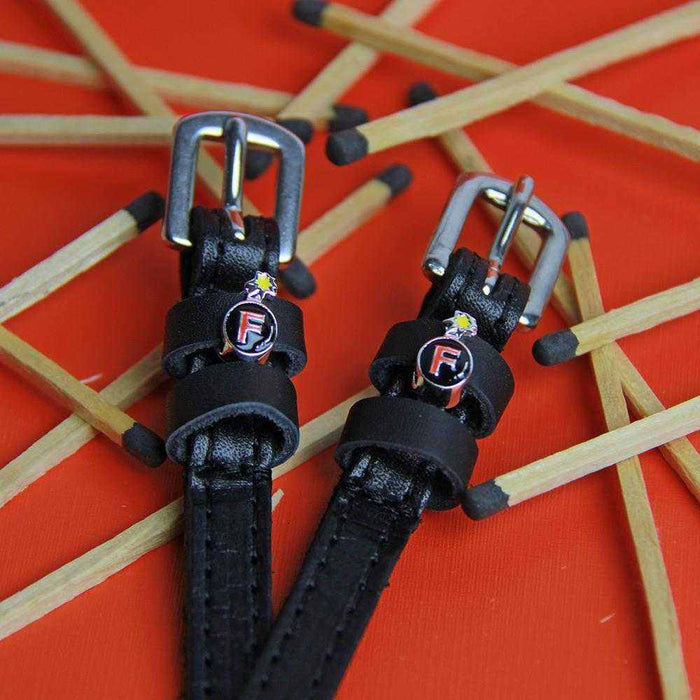F Bomb spur straps with red bomb charms styled among scattered matchsticks on orange