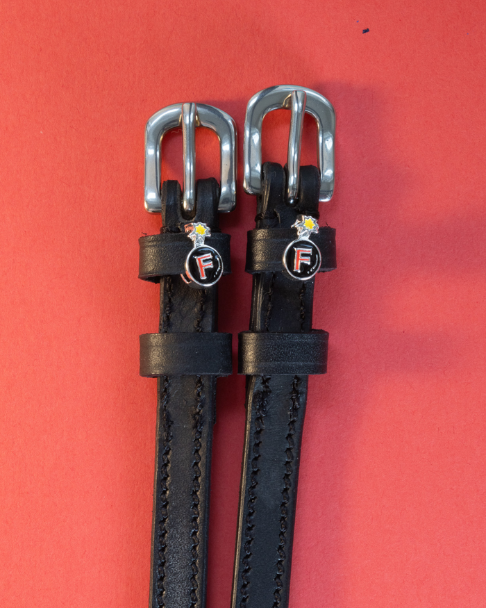 Pair of black leather F Bomb spur straps with silver buckles on a coral background