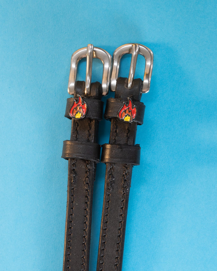 Black leather ManeJane spur straps with silver buckles and red flame charms on light blue