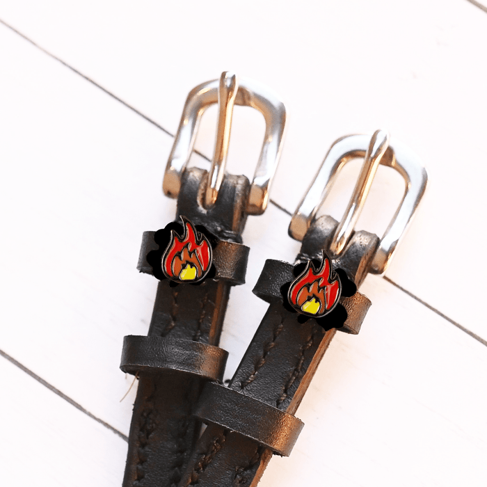 Close-up of red-and-orange flame charms on dark leather spur straps on white wood