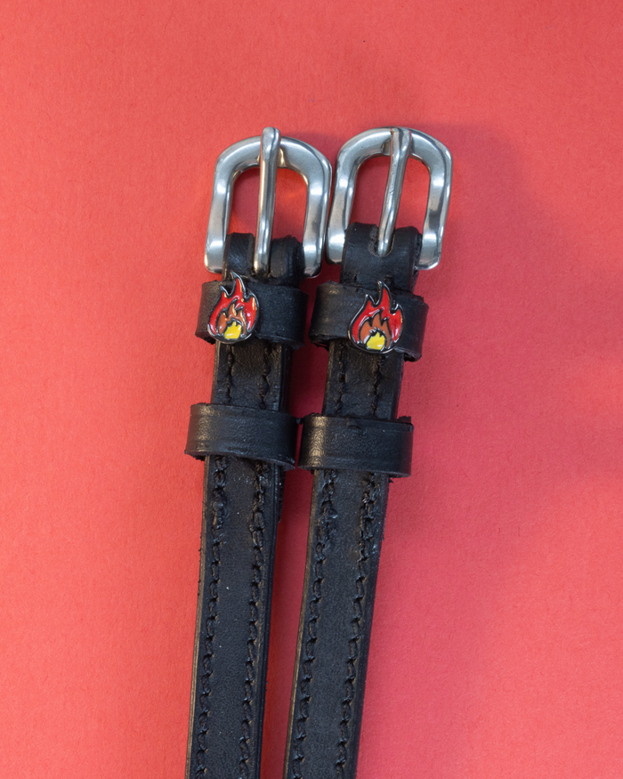 Black leather flame charm spur straps with silver buckles on a red background