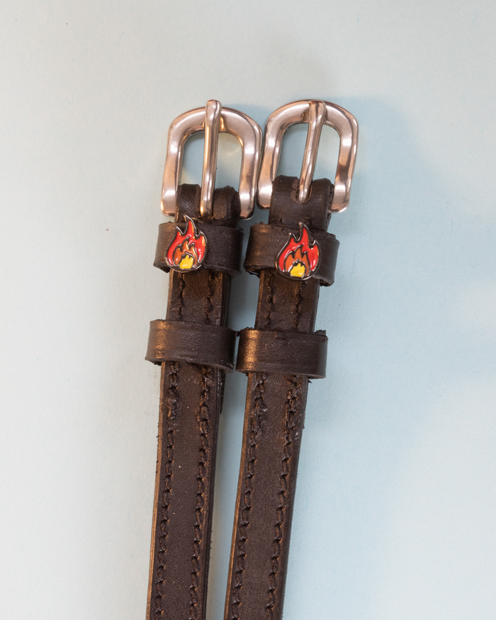 Brown leather flame spur straps with rose-gold buckles and fire charms, flat-lay