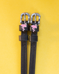 Black leather ManeJane flamingo spur straps with silver buckles on a yellow background