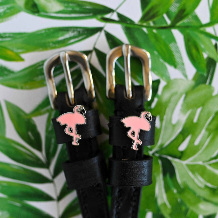 Flamingo charm spur straps against a tropical palm-leaf print background