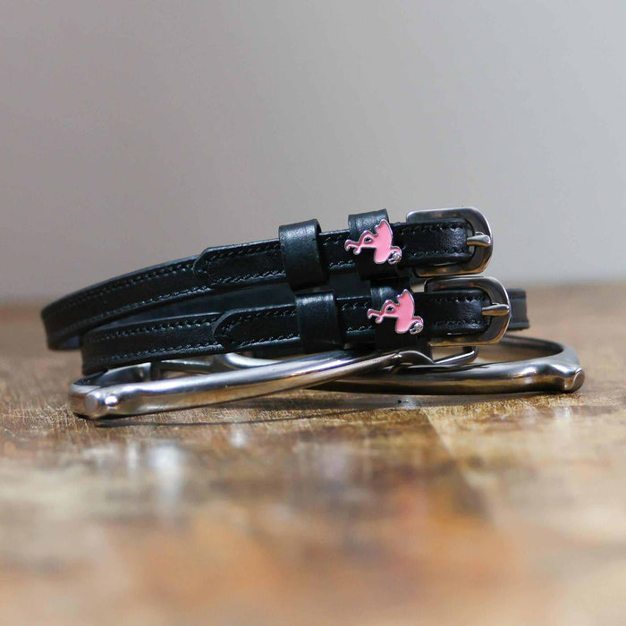 Black leather flamingo spur straps coiled beside a stirrup on wood