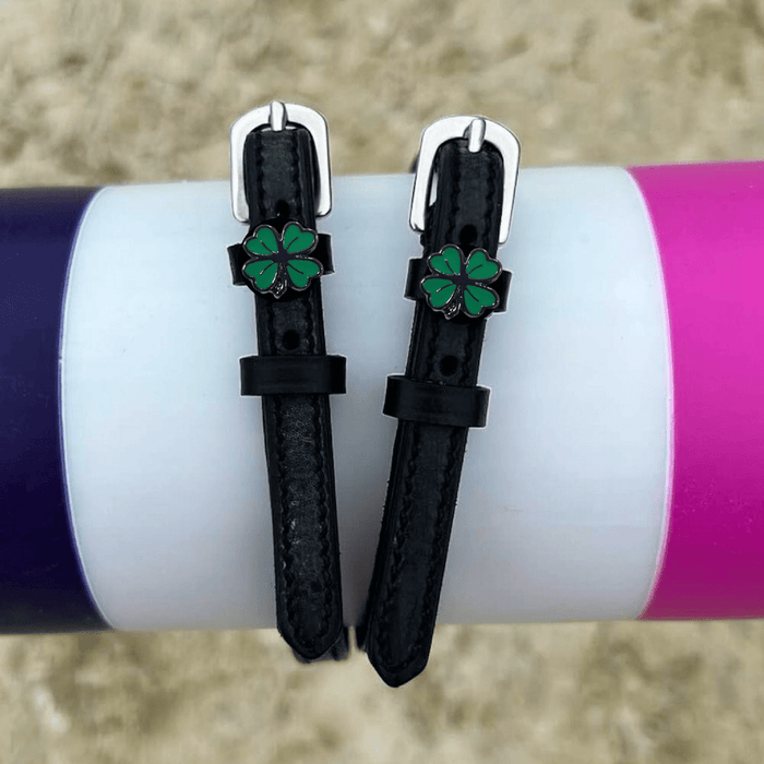 Four leaf clover spur straps draped over a purple and pink jump rail, green clover charms