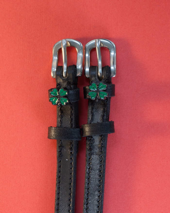 ManeJane clover spur straps with silver buckles flat on a red background, green clover charms