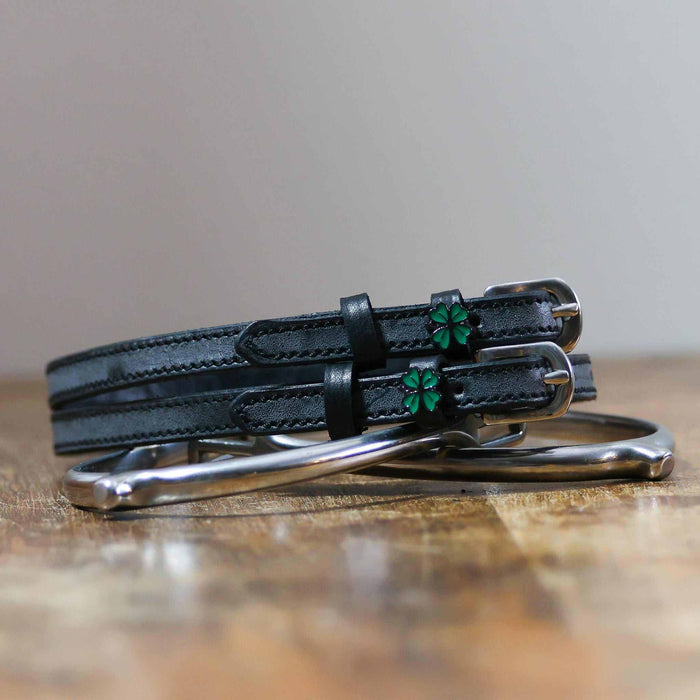 Coiled black leather clover spur straps resting on a silver spur, green four leaf clover charms