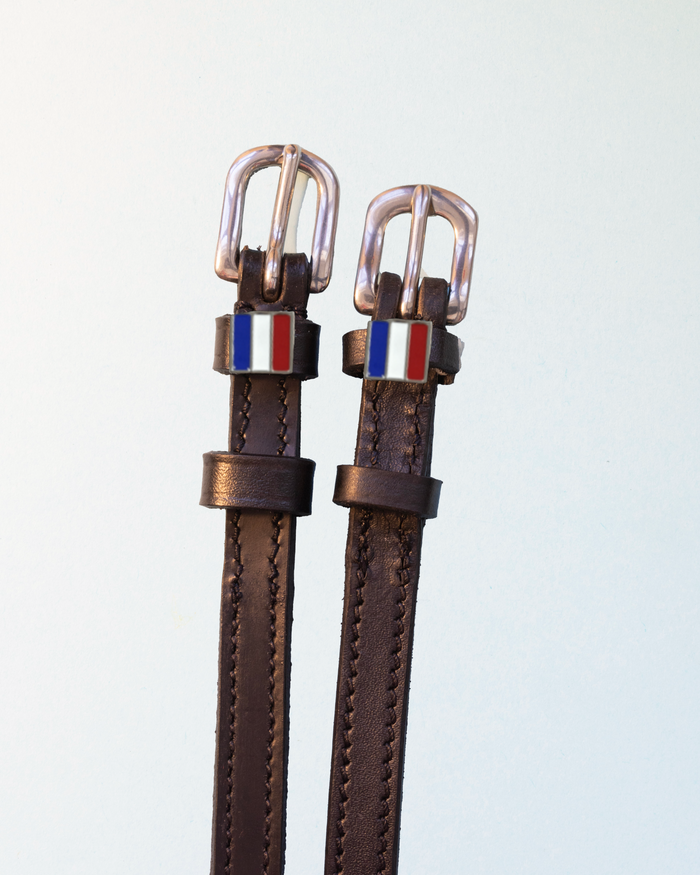 Brown leather ManeJane spur straps with rose gold buckles and French flag charms on white