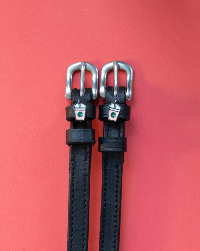 Black leather ManeJane spur straps with silver frappe cup charms on a red background