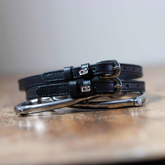 Coiled black leather spur straps and a silver spur on wood with frappe cup charms