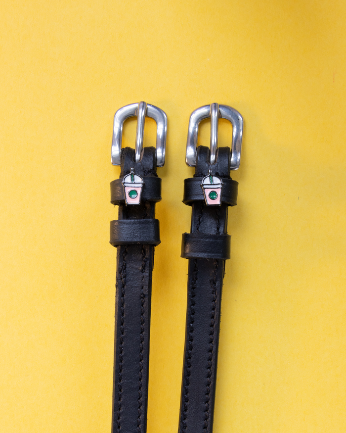Black leather frappe cup spur straps laid flat on a yellow background