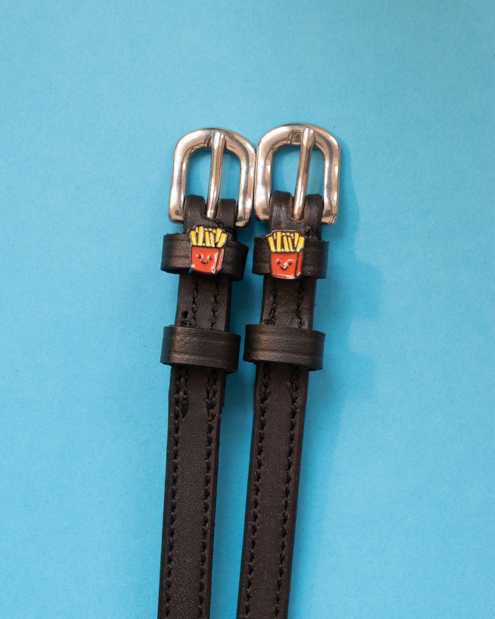 Pair of black leather French fry charm spur straps with silver buckles on light blue