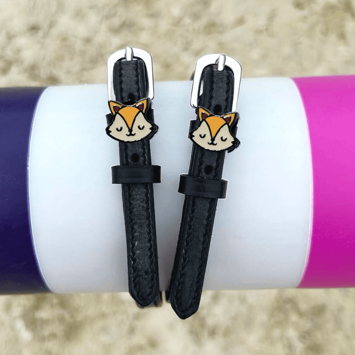 Black leather fox spur straps styled over colorful tumblers on sand by ManeJane
