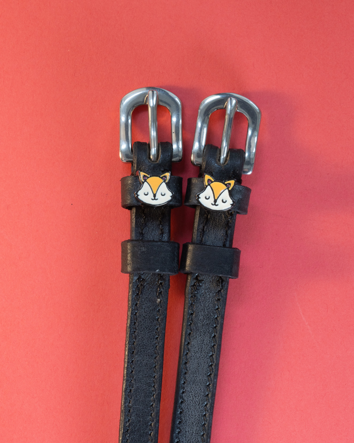 Pair of black leather fox face spur straps with silver buckles on a coral background