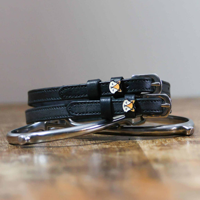 Coiled black leather ManeJane fox spur straps stacked on a silver spur on wood