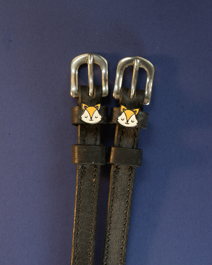 Black leather spur straps with orange fox face charms on a dark navy background