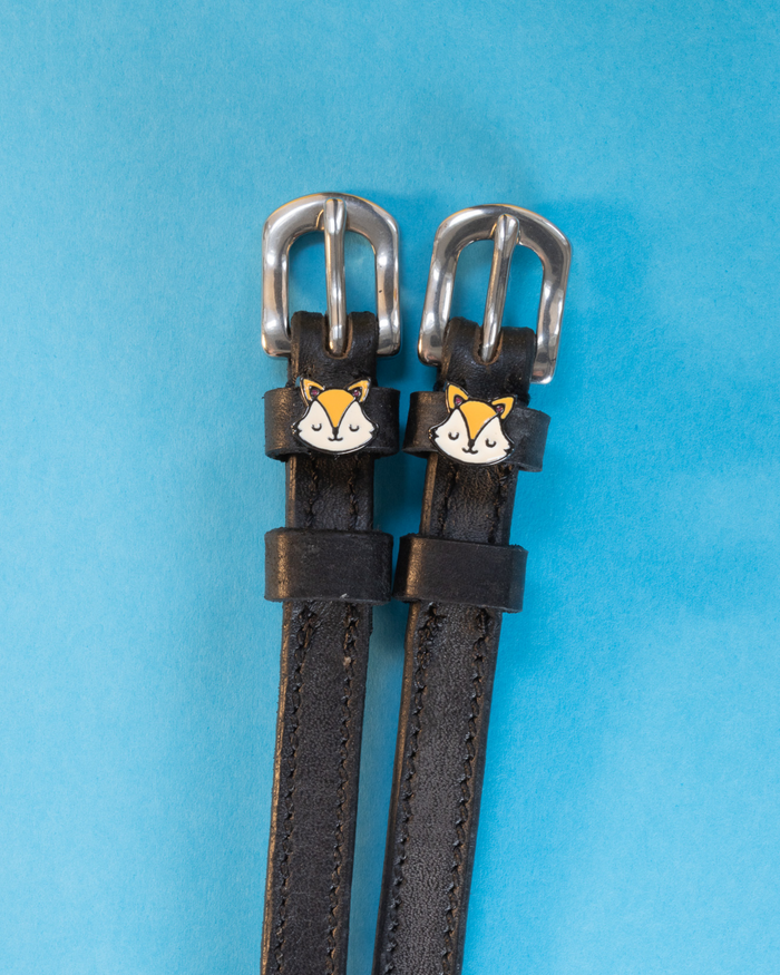 Black leather ManeJane fox spur straps with silver buckles on a bright blue background