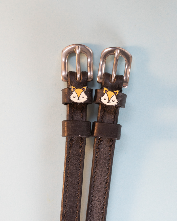 Brown leather fox face spur straps with silver buckles on a pale blue background