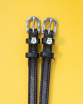 Black leather ManeJane spur straps with silver buckles and green frog charms on a yellow background
