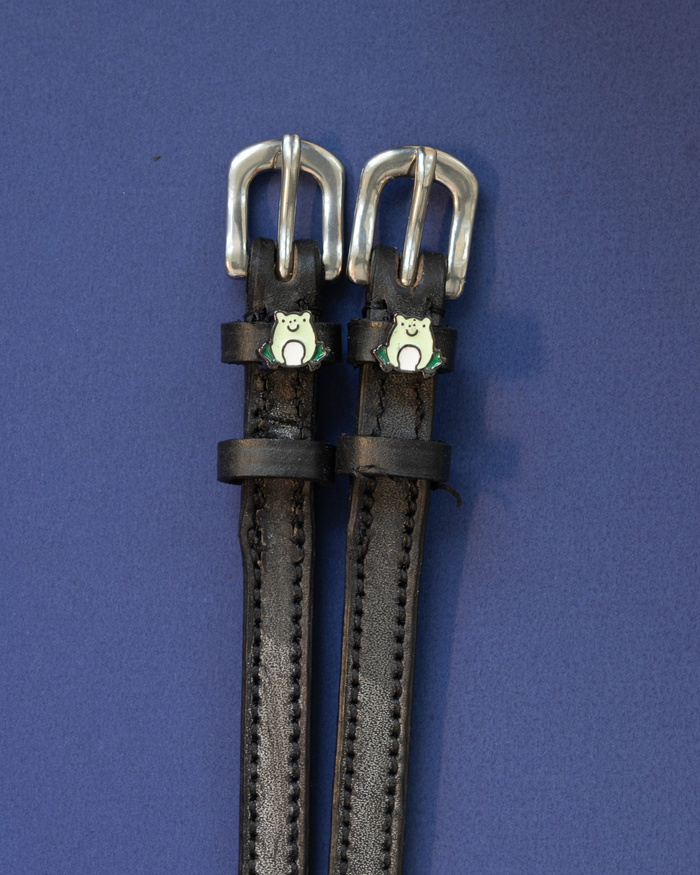 Pair of black leather ManeJane frog spur straps with silver buckles on a deep blue background