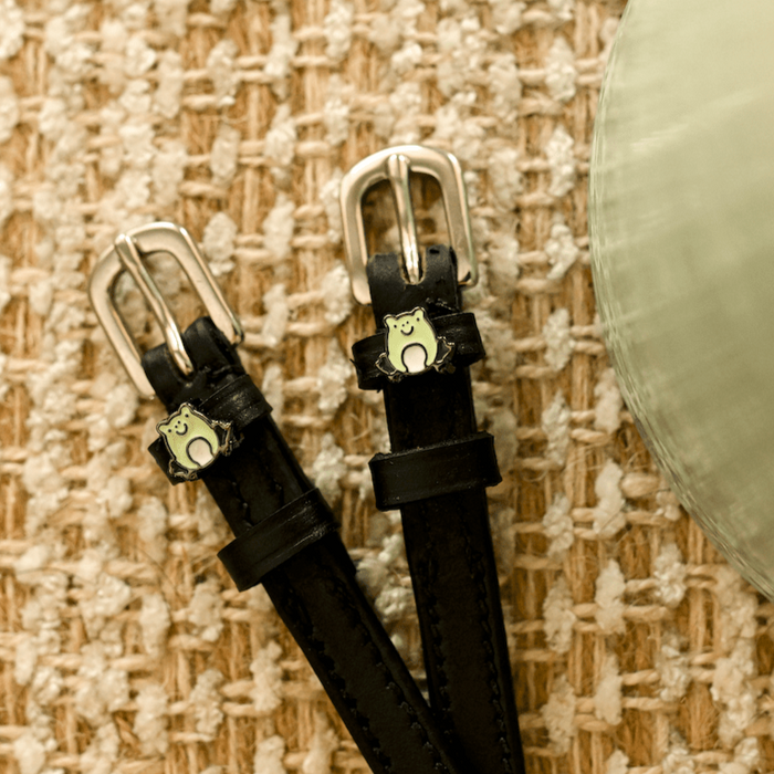 Black leather frog spur straps with silver buckles angled on a woven jute background