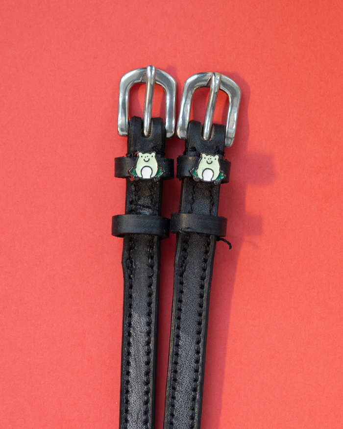 Black leather frog spur straps with silver buckles flat-laid on a bright red background