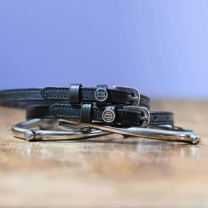 Stacked black Gemini spur straps with silver buckles on wood, round zodiac charm, ManeJane